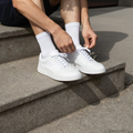 Homme nouant ses baskets blanches avec des chaussettes basses blanches